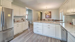 A modern kitchen with white cabinetry, a stainless steel refrigerator, and a marble countertop. - Updated Family Getaway: Walk to Sea Haven Beach! (Sneads Ferry)