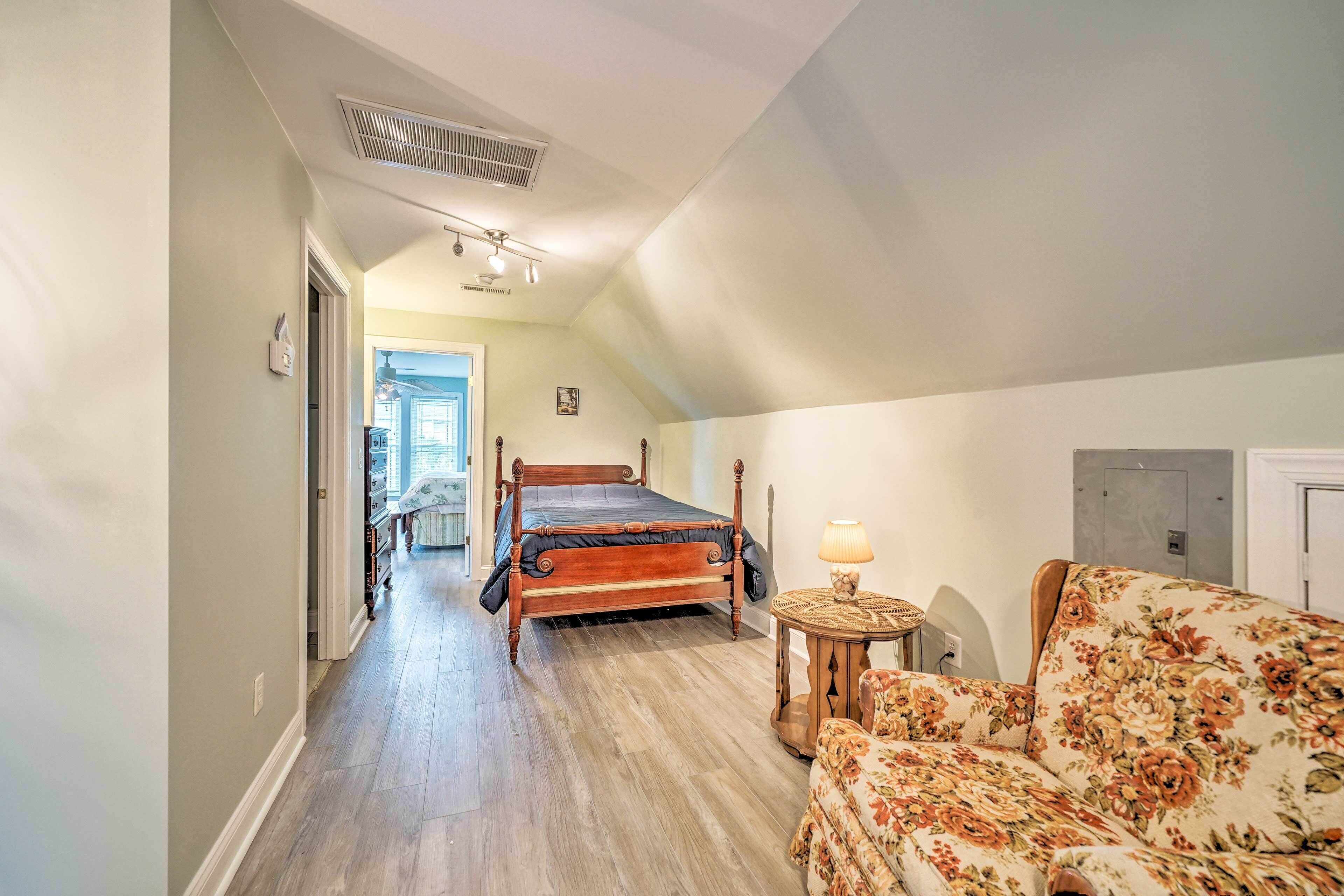 A bedroom with a wooden bed, a floral sofa, a round side table, and a view of the hallway.