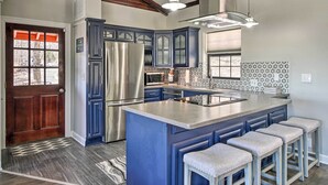 Eine moderne Küche mit blauen Schränken, einem Edelstahlkühlschrank und einer großen Kochinsel mit Barhocker.
