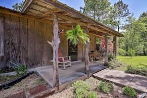 A rustic wooden building with a covered porch, a red chair, and a hanging fern. - Secluded Cabin w/ Pond ~ 37 Mi to Gulf Coast! (Wiggins)