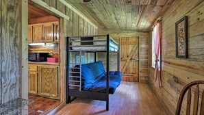 Un lit superposé dans une cabane en bois, avec un coin cuisine et une fenêtre.