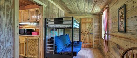 Cama litera en una cabaña de madera con una zona de cocina y una ventana.