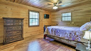 Une chambre aux murs lambrissés, avec un lit, une commode et un ventilateur de plafond.