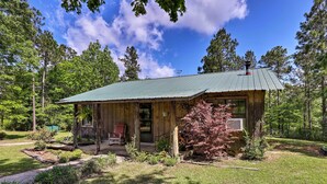 Une cabane rustique avec un toit en métal vert, entourée d’une pelouse bien entretenue et d’arbres.