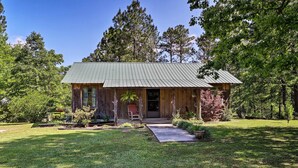 Une cabane rustique avec un toit en métal, entourée d’une pelouse bien entretenue et d’arbres denses.