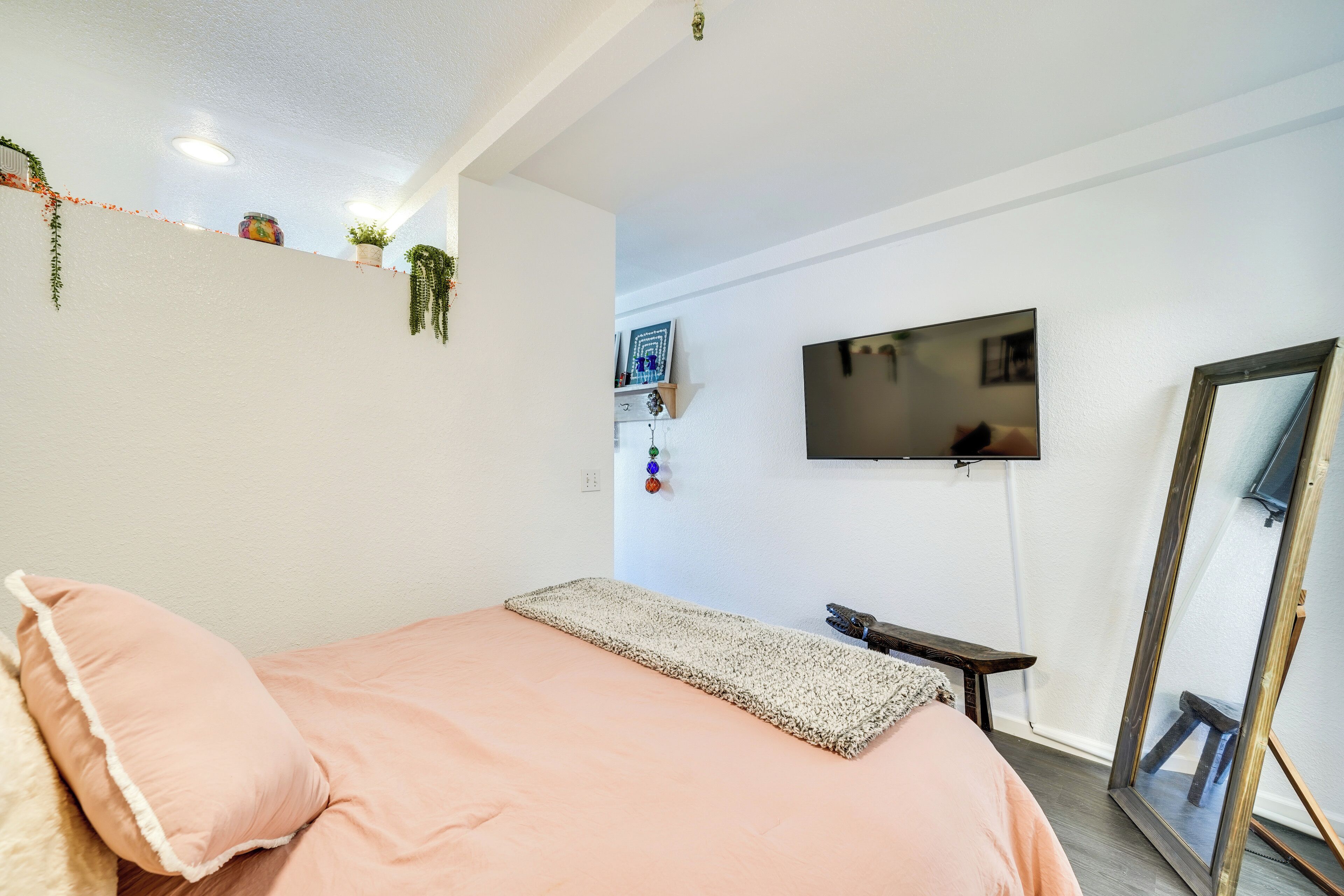 A bedroom with a bed, a TV mounted on the wall, a mirror, and a small table.