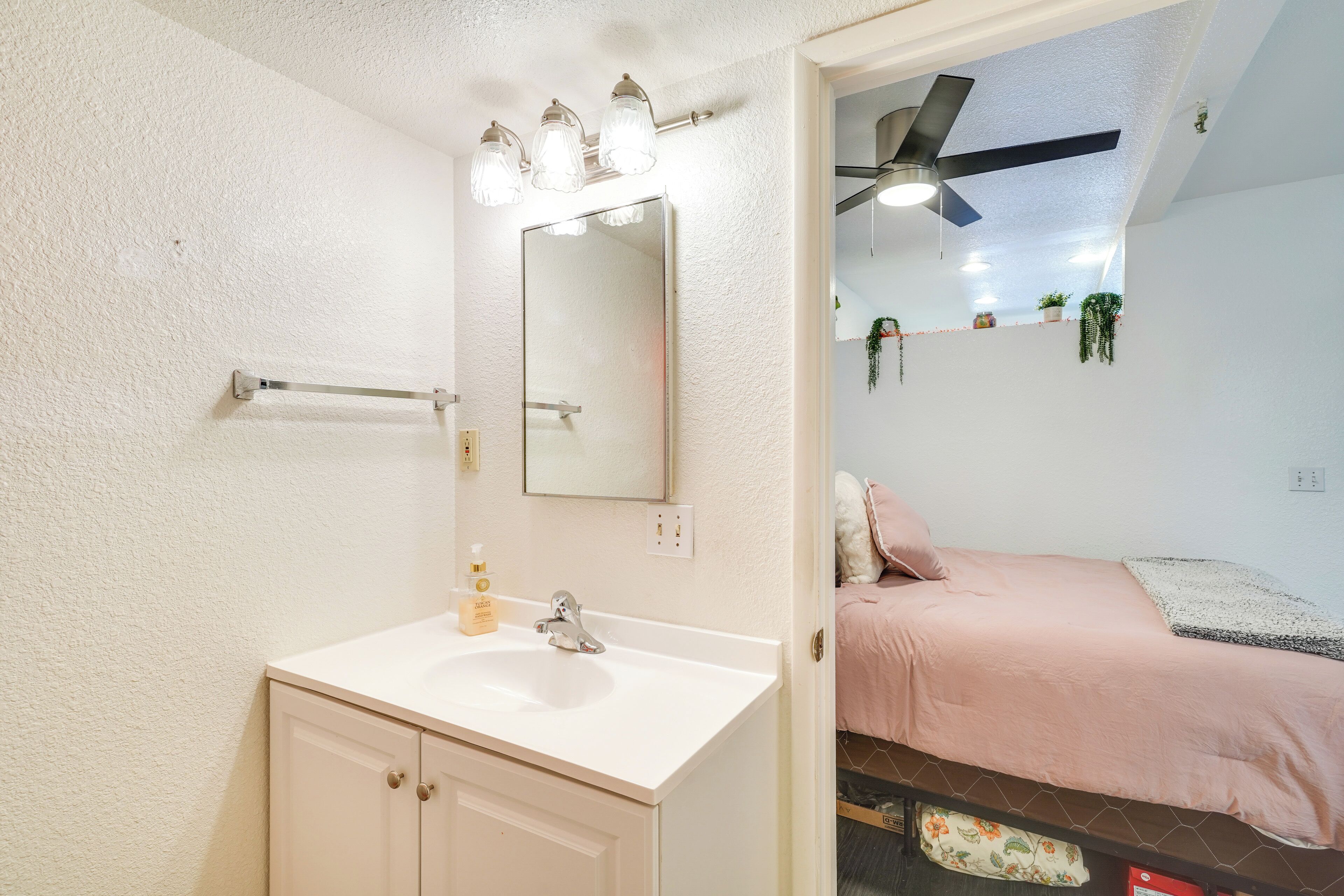Une salle de bain avec un lavabo blanc, un miroir et un ventilateur de plafond.