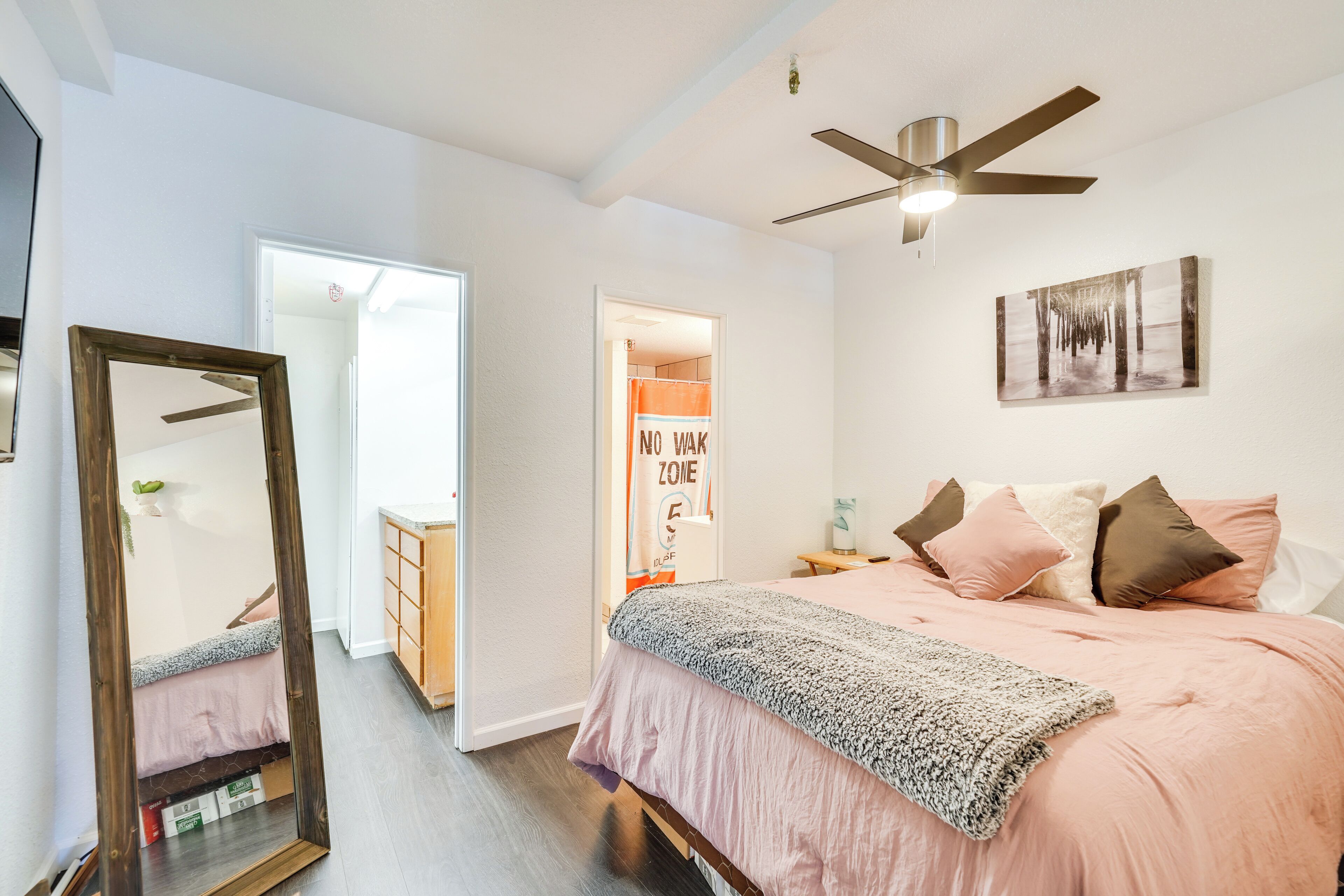 Un dormitorio con una cama, un ventilador de techo, un espejo, una puerta y una obra de arte en la pared.