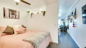Een slaapkamer met een bed, een plafondventilator, een tv aan de muur en een gang naar een zithoek.
