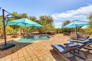 Una piscina con lettini e ombrelloni, circondata da rocce e palme.