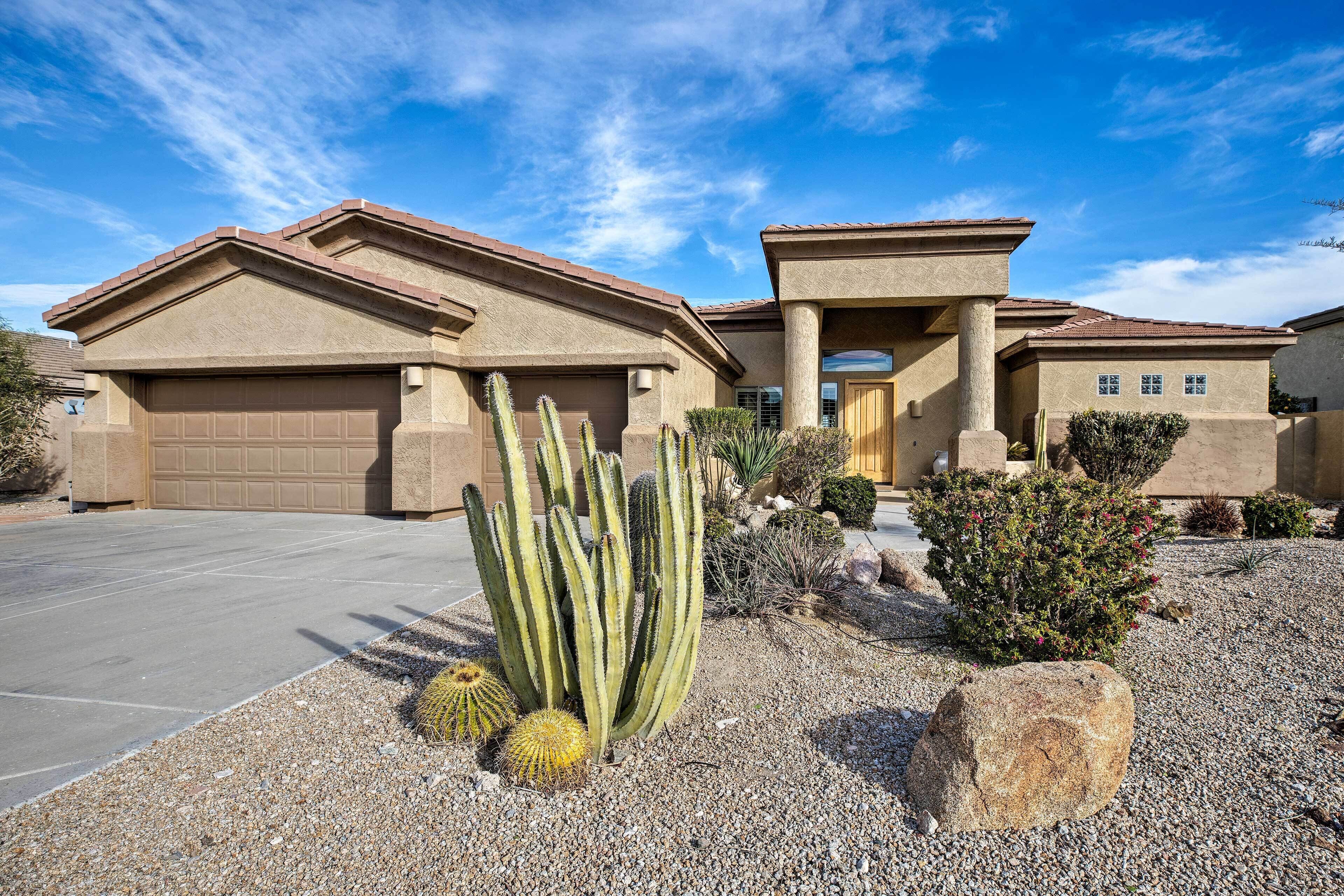 Une maison d’habitation avec un garage, une allée et un jardin de style désertique agrémenté de cactus et de rochers.