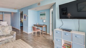 A living room with a sofa, a desk, and a TV. There is a bookshelf and a game box on the desk. - Oceanfront Myrtle Beach Condo With Resort Perks! (Myrtle Beach)