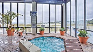 An indoor swimming pool with a view of the beach, surrounded by potted plants and safety signs. - Oceanfront Myrtle Beach Condo With Resort Perks! (Myrtle Beach)
