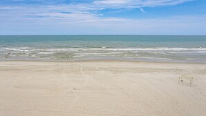 A beach with a sandy shore and a small yellow structure, likely a lifeguard stand, in the distance. - Oceanfront Myrtle Beach Condo With Resort Perks! (Myrtle Beach)