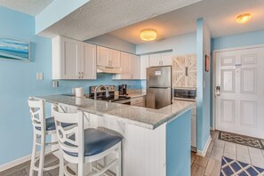 A kitchen with white cabinets, a stainless steel refrigerator, and a marble countertop.