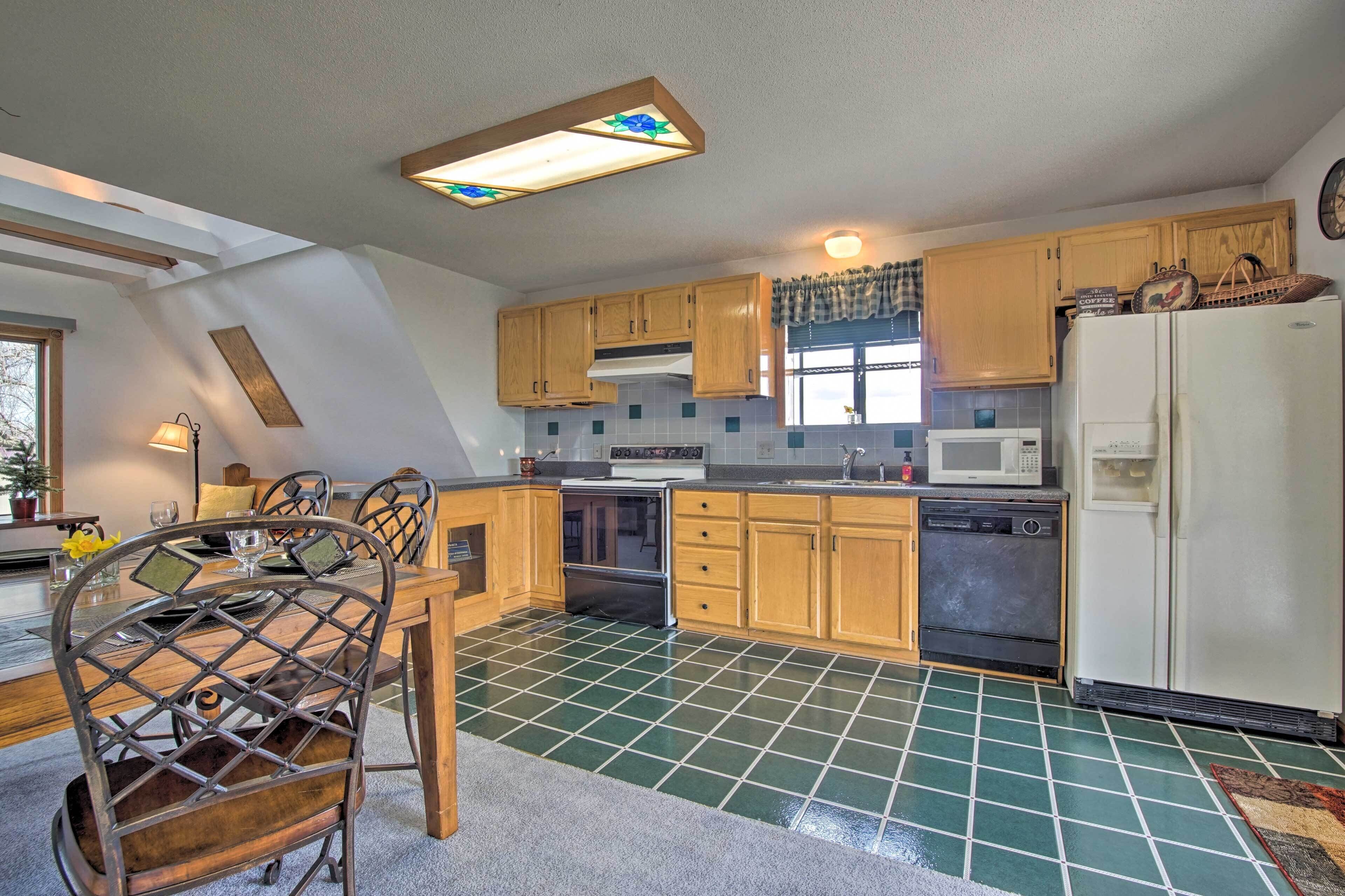 Una cocina con armarios de madera, un refrigerador, un microondas y un comedor con mesa y sillas.