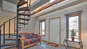 Un vaste espace de vie agrémenté d’un escalier en bois, d’un canapé coloré et d’une porte donnant sur l’extérieur.