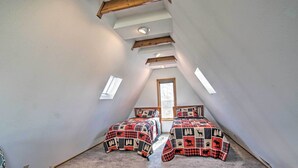 Une chambre avec deux lits, un plafond en pente et une fenêtre.
