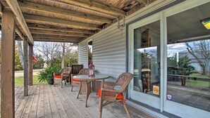 Une terrasse couverte avec un plancher en bois, des meubles en osier et une porte vitrée donnant sur un jardin.