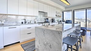 A modern kitchen with white cabinets, a marble island, and a large window offering a city view. - Luxury Long Beach Villa With Ocean Views! (Long Beach)