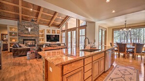 A spacious kitchen with a large island, wooden cabinetry, and a stone fireplace. - Fire Pit: Family-friendly Lakeside Retreat (Lakeside)