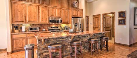 A kitchen with wooden cabinets, a stone island, stainless steel appliances, and a trash can.