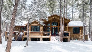 A wooden cabin with a porch and large windows, surrounded by snow-covered trees.