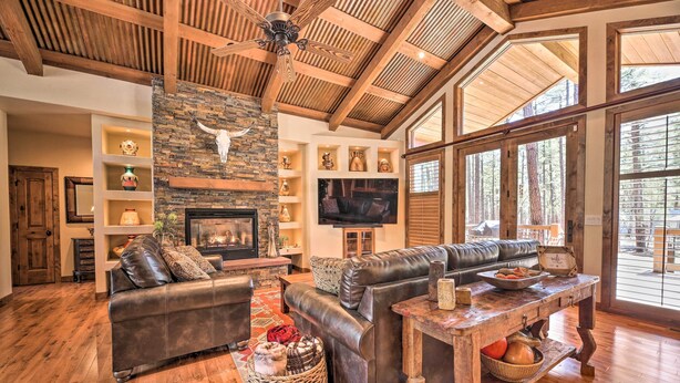 A spacious living room with a fireplace, leather sofas, a wooden coffee table, and large windows offering a view of the outdoors. - Fire Pit: Family-friendly Lakeside Retreat (Lakeside)