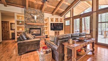 A spacious living room with a fireplace, leather sofas, a wooden coffee table, and large windows offering a view of the outdoors.