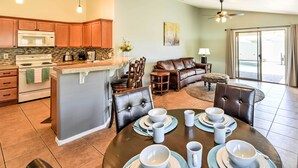 A modern kitchen with a central island, dining area with a round table and chairs, and a living room with a sofa and a coffee table. - Serene Surprise Home w/ Backyard & Private Pool (Surprise)
