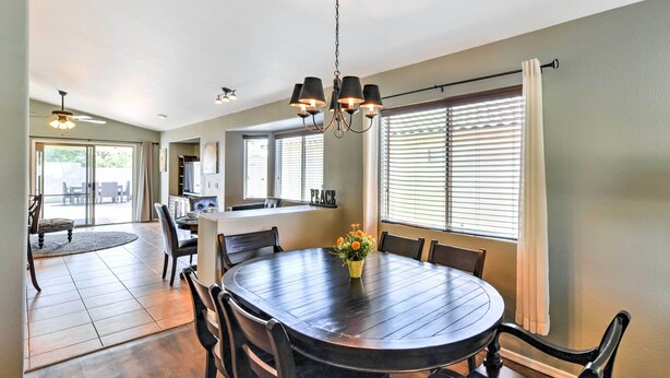 A dining area with a round table, chairs, and a chandelier. There is a window with blinds and a view of the outdoors. - Serene Surprise Home w/ Backyard & Private Pool (Surprise)