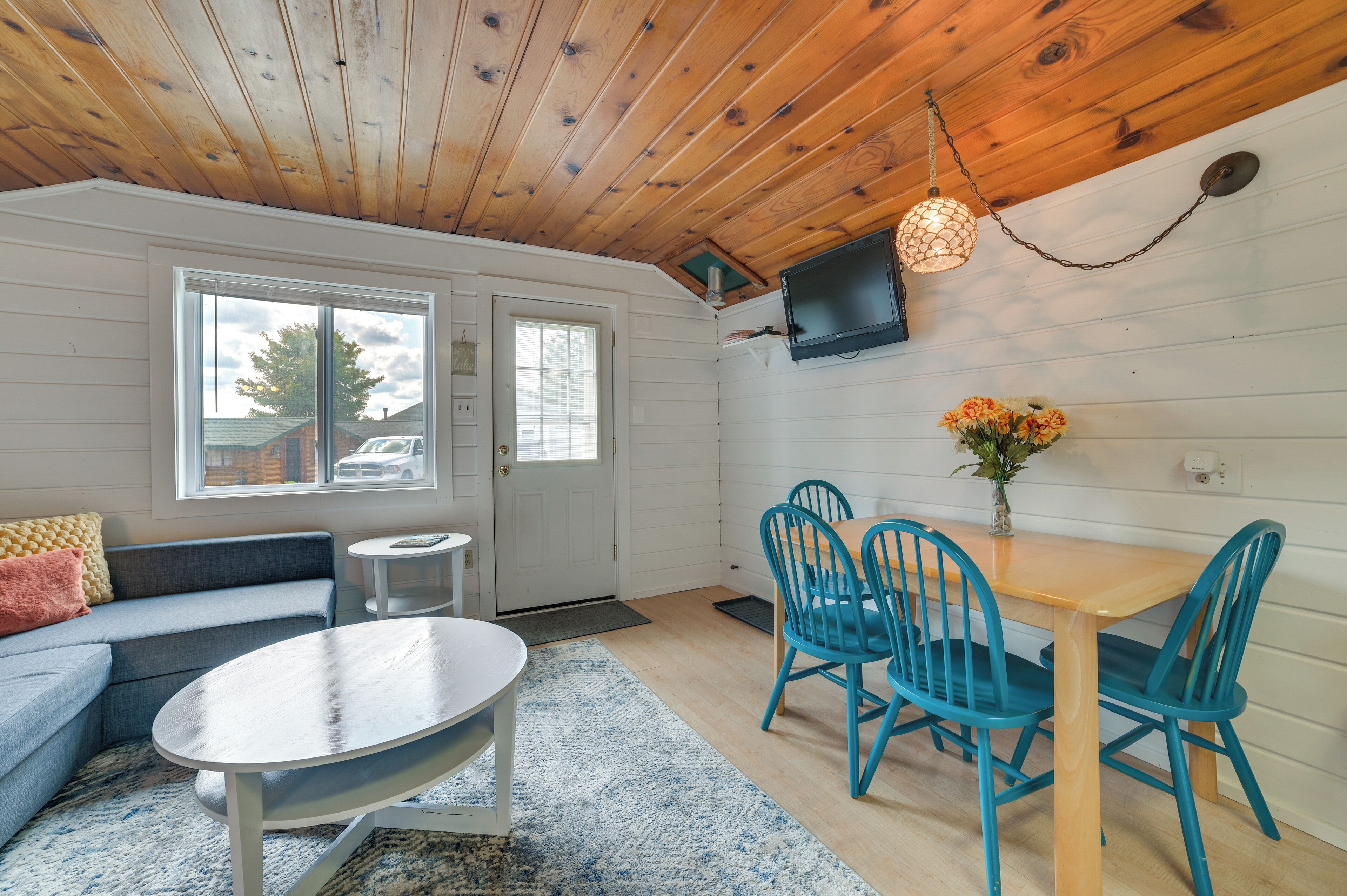 Una habitación acogedora con techo de madera, un sofá, una mesa redonda y un comedor con sillas azules.