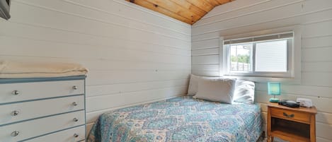 Un dormitorio con una cama, un aparador, una mesita de noche, una ventana y un ventilador de techo.