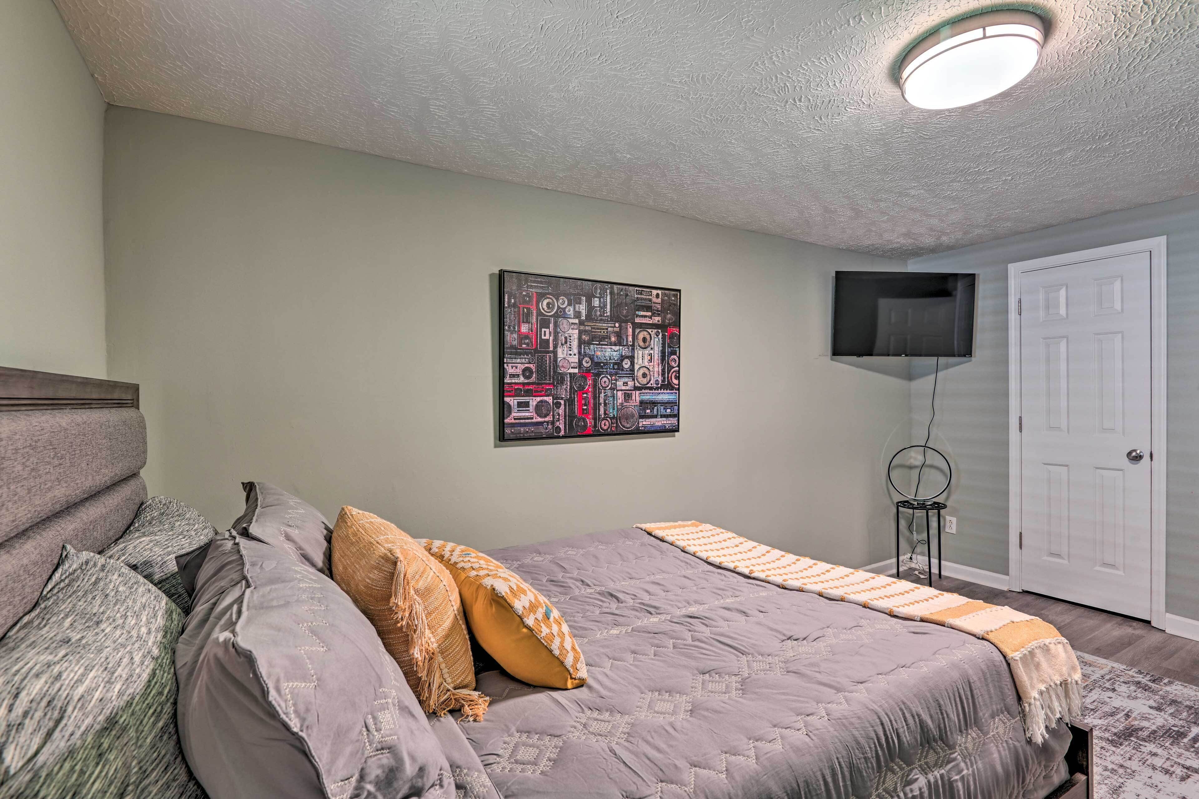 Une chambre à coucher avec un lit, des oreillers, un téléviseur fixé au mur et une porte.