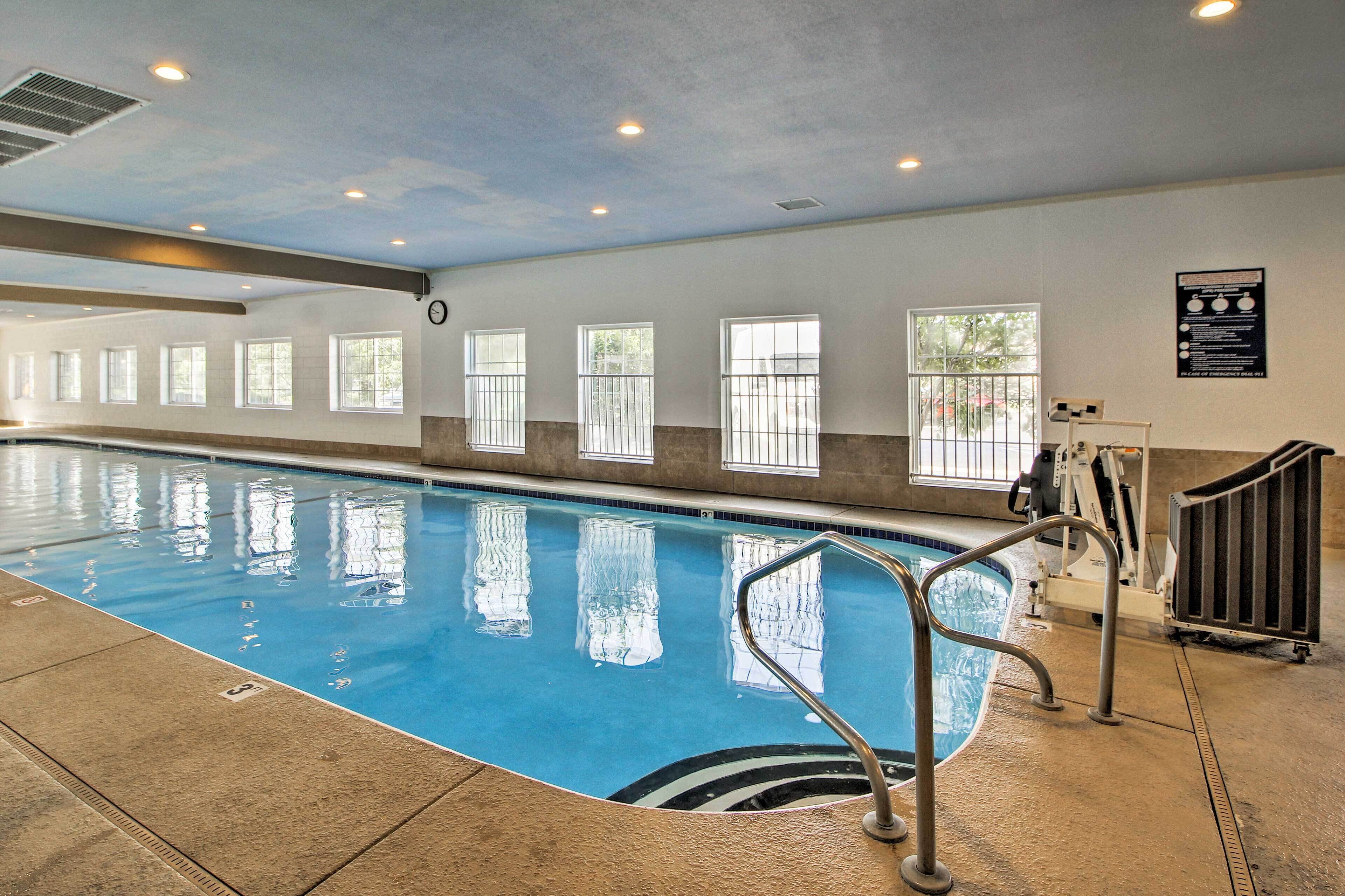 An indoor swimming pool with clear water, a tiled floor, and windows along the walls.