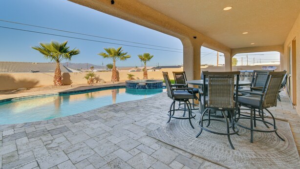 Un espace extérieur avec piscine et jacuzzi, entouré de palmiers et agrémenté d’une terrasse avec des chaises et une table.