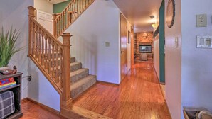 A wooden staircase leading to a second floor, a hallway with wooden flooring, and a kitchen area visible through an open door. - Deck + Yard: Family-friendly Pinetop Retreat (Pinetop)