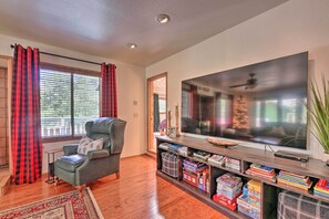 A living room with a large flat-screen TV, a leather armchair, and a bookshelf filled with books. - Deck + Yard: Family-friendly Pinetop Retreat (Pinetop)