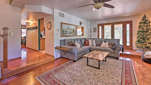 A spacious living room with a large sectional sofa, a wooden coffee table, and a Christmas tree. - Deck + Yard: Family-friendly Pinetop Retreat (Pinetop)