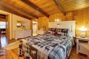 Ein Schlafzimmer mit karierter Bettdecke, Holzwänden, einem weißen Schminktisch und einem Nachttisch mit Lampe sowie einem Spiegel an der Wand.