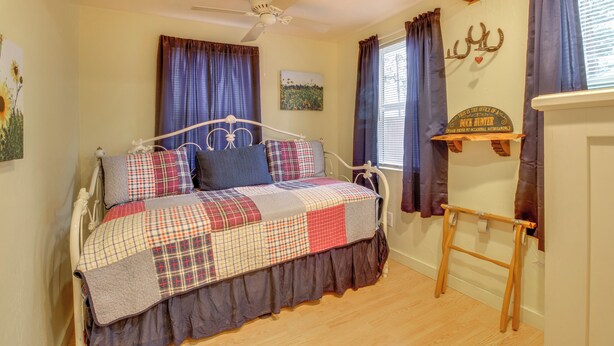 A bedroom with a bed, a ceiling fan, a window with curtains, a wall-mounted shelf, and a rustic decor piece. - White Mountains Hideaway! Family Cabin in Lakeside (Lakeside)