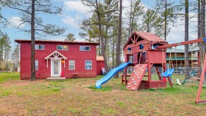 A red playhouse with a slide and climbing wall, surrounded by trees. - White Mountains Hideaway! Family Cabin in Lakeside (Lakeside)