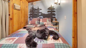 A cozy room with a bed, a wooden headboard, a wall clock, and a nightstand. - White Mountains Hideaway! Family Cabin in Lakeside (Lakeside)