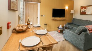 Un comedor con una mesa de madera preparada para dos personas, un sofá, un televisor de pantalla plana y una lámpara.