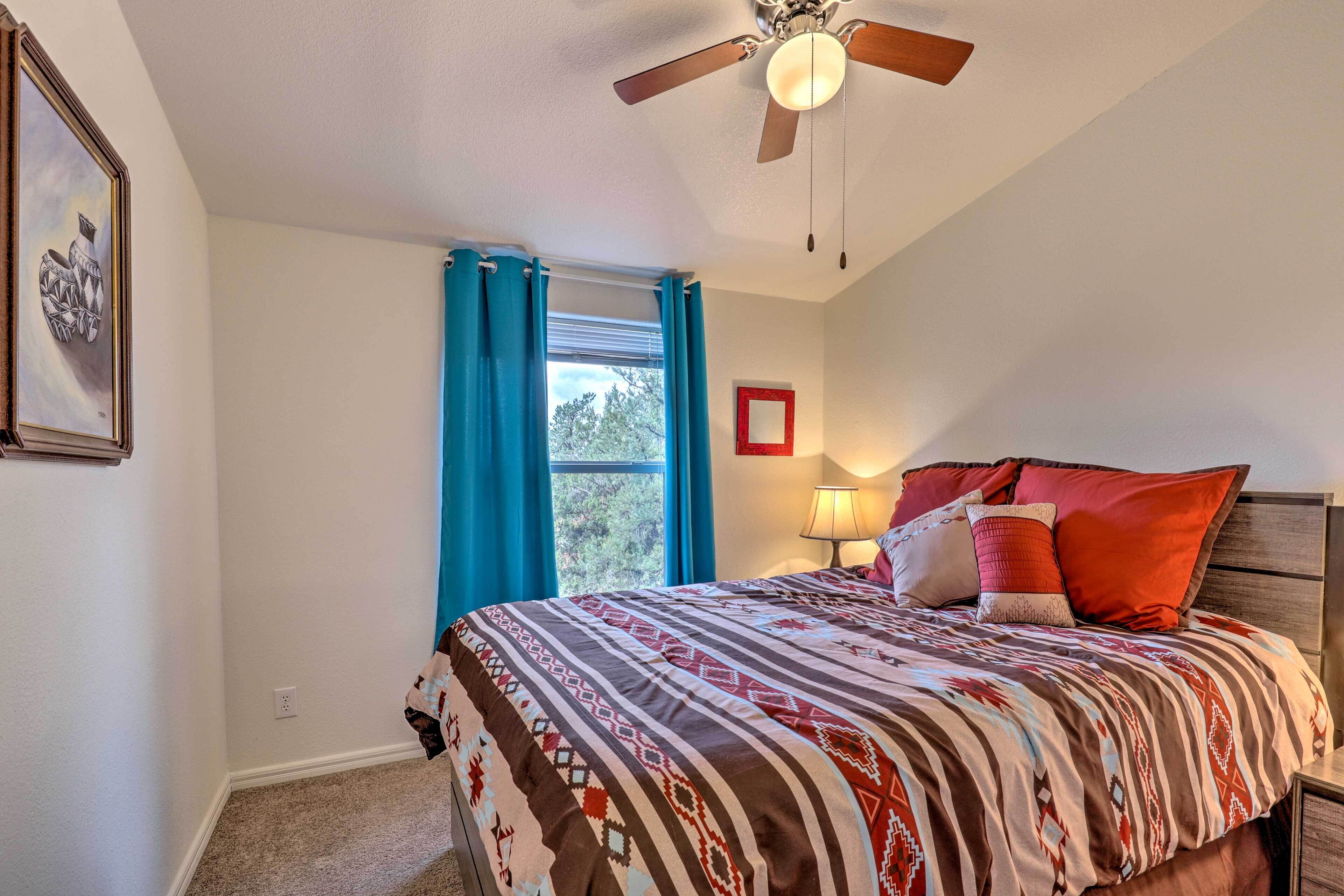 A bedroom with a bed, a ceiling fan, a window with curtains, and a framed picture on the wall.