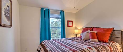 A bedroom with a bed, a ceiling fan, a window with curtains, and a framed picture on the wall.