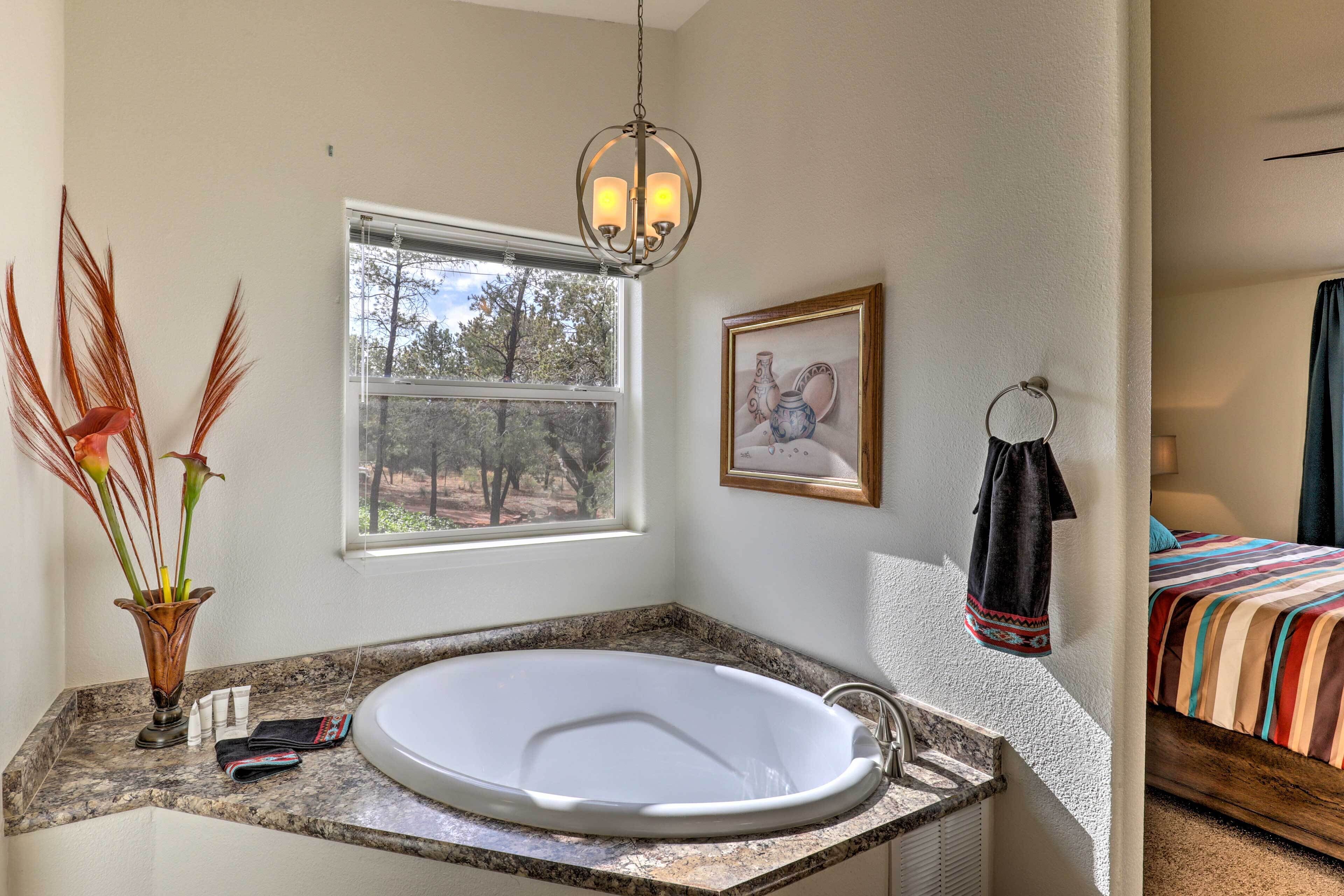 A bathroom with a large bathtub, a window, a framed picture, and a towel rack.