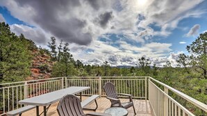 Eine Terrassenausrichtung mit Picknicktisch und zwei Adirondack-Stühlen, umgeben von einem Geländer und mit Blick auf ein bewaldetes Gebiet.