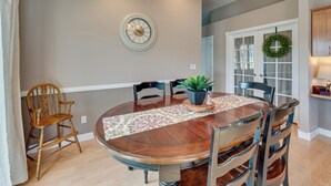 A dining room with a round wooden table, six chairs, a potted plant, and a clock on the wall. - Pet-friendly Nampa Vacation Rental With Yard! (Nampa)