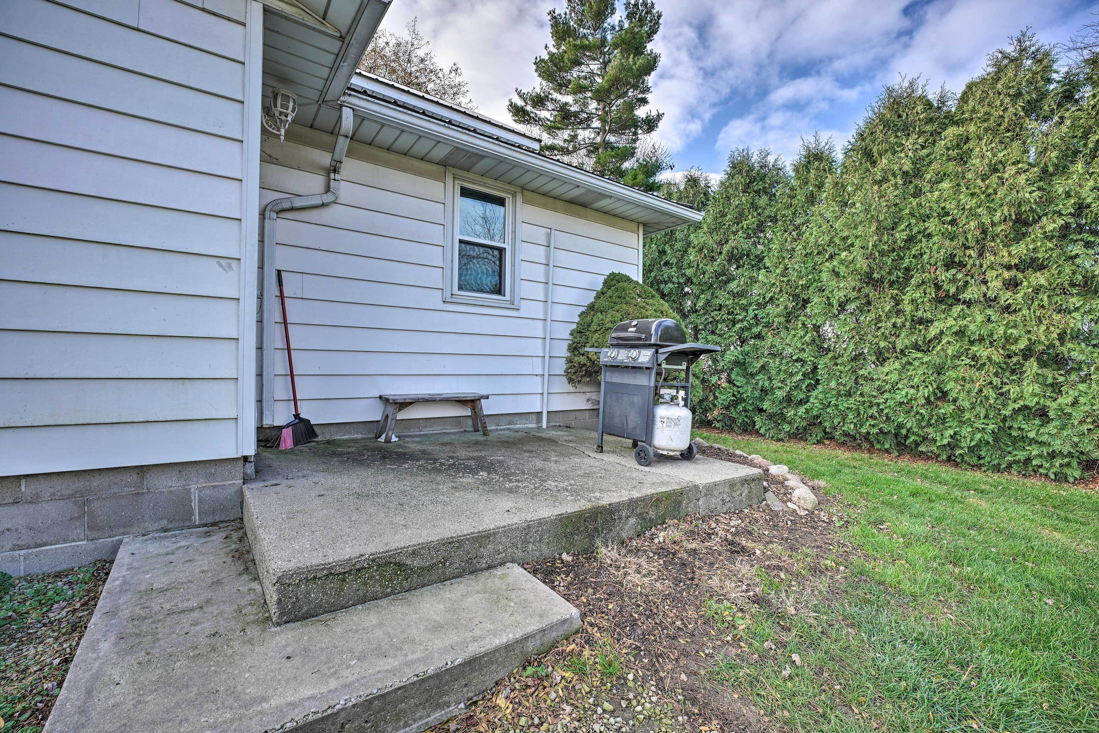 A house with a concrete porch, a gas grill, and a hedge.